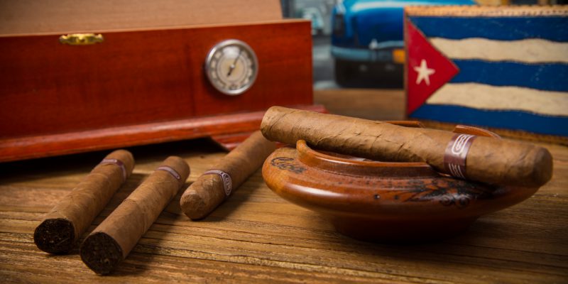 cigars and humidor Cuban cigars and humidor with ashtray on rustic wooden table with Cuban painting of american old car in background